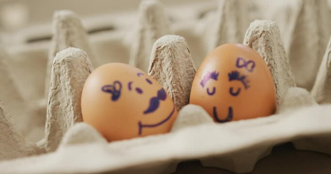 Video of close up of two brown eggs with drawn faces in egg carton background
