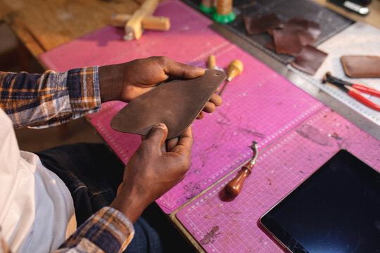High angle midsection of african american young craftsman holding leather at table in workshop - Powered by Adobe