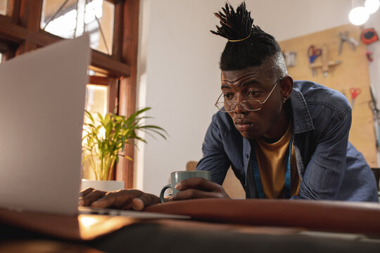 African american young craftsman using laptop at table in leather workshop
