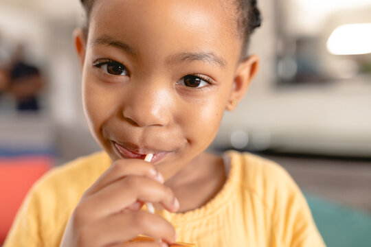 Close-up portrait of cute african american girl eating lollipop at home