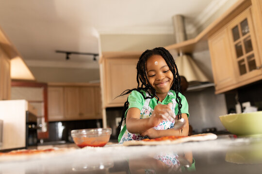 Smiling cute african american girl with black braids making pizza at kitchen counter