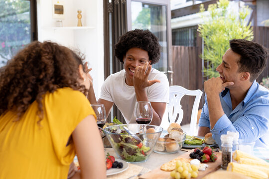 Cheerful multiracial friends enjoying lunch while sitting together at dining table
