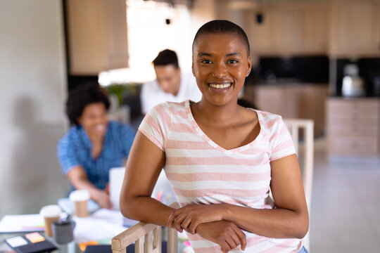 Portrait of smiling young biracial businesswoman standing against colleagues at home office
