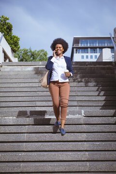 Happy african american mid adult businesswoman talking on phone while moving down steps in city
