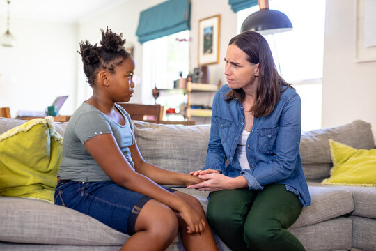 Caucasian mature woman scolding african american daughter while sitting on sofa at home