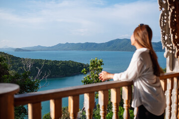 Blurred rear view image of a young woman looking at an islands and a beautiful sea view from resort terrace