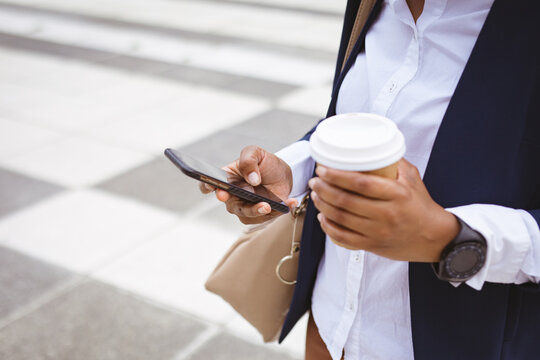 Midsection of african american mid adult businesswoman holding disposable cup while using phone