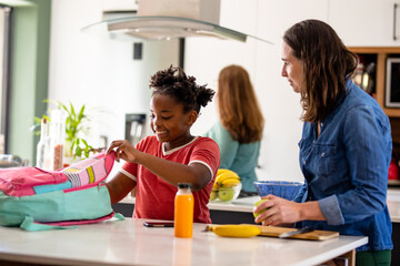 Caucasian mature woman looking at african american girl packing school bag at table