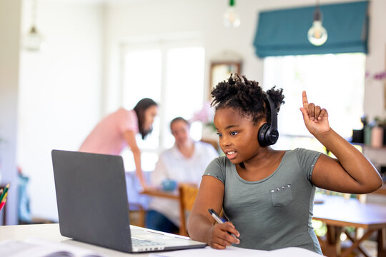 African american girl raising hand while attending online school on laptop at home