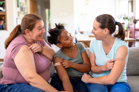 Smiling caucasian mature lesbian couple and african american daughter showing vaccinated bandage