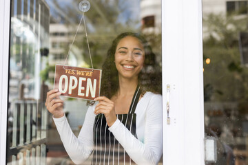 Smiling african american barista hanging open sign on glass door in coffee shop