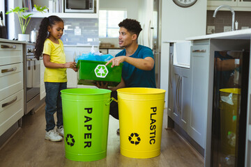 Biracial father teaching recycling waste to daughter in kitchen at home
