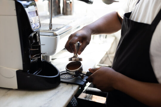 Midsection of male african american barista using portafilter while making coffee at cafe