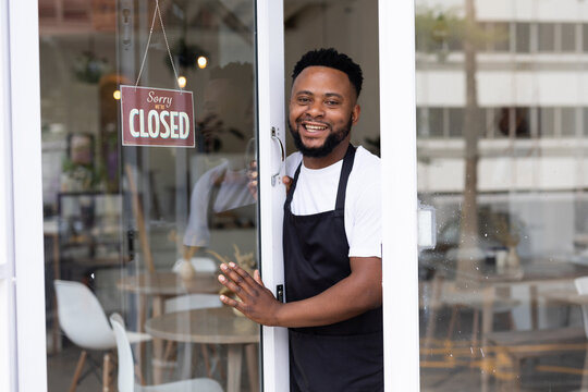Smiling portrait of african american male barista standing at coffee shop doorway with open sign
