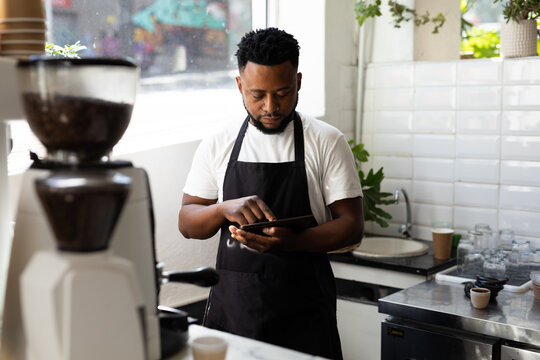 Young male african american barista using tablet pc while working in coffee shop