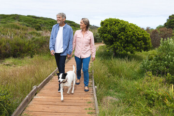 Happy caucasian mature couple looking away while walking with dog on boardwalk
