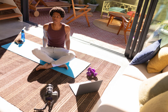 African american young man sitting on exercise mat while making vlog at home