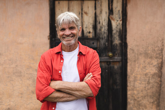 Portrait of happy caucasian mature man standing with arms crossed against house