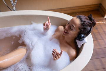 High angle view of biracial young woman enjoying music through headphones in bathtub at spa
