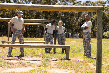 Group of diverse male and female soldiers standing at wooden hurdles obstacle course in boot camp