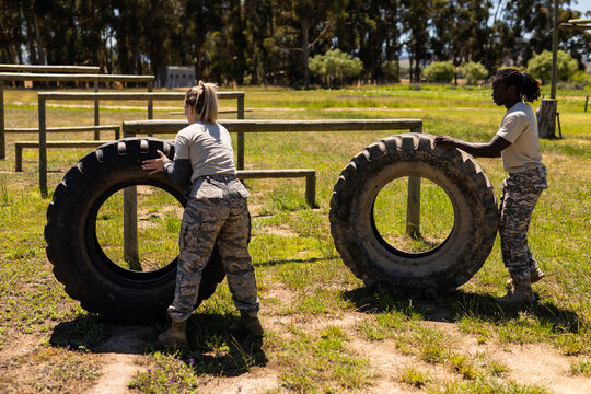 Diverse male and female soldiers rolling a tire during obstacle course at boot camp