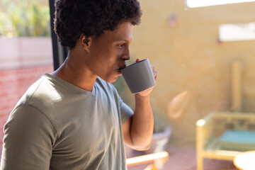 Close-up of african american young man drinking coffee while standing by window at home