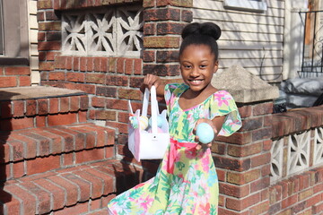 Happy little girl holding easter egg and basket standing on front step of city home