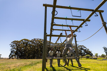 Caucasian male soldier climbing monkey bars during obstacle course at boot camp