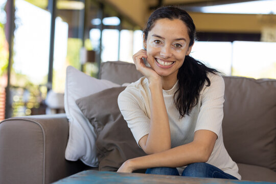 Portrait of happy biracial young woman with hand on chin sitting on sofa at home