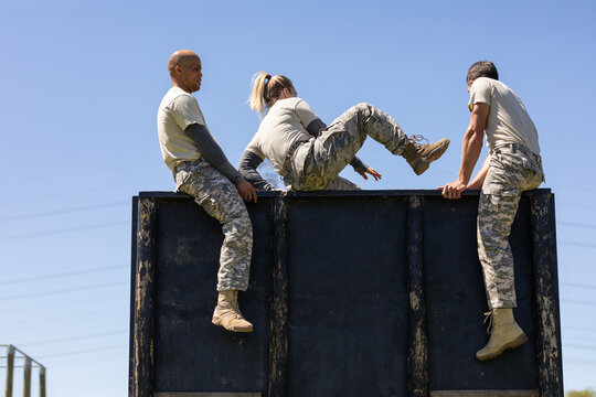 Two diverse male and female soldiers climbing wooden wall during obstacle course at boot camp
