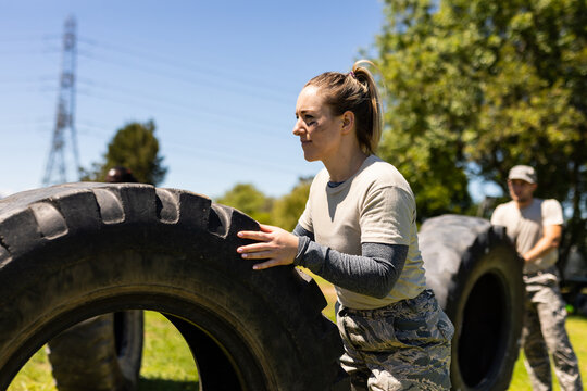 Caucasian female soldier rolling a tire during obstacle course at boot camp