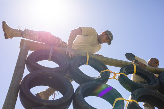 Two diverse male soldiers climbing a tire wall during obstacle course at boot camp