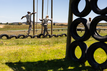 Diverse male and female soldiers walking on tires during obstacle course at boot camp
