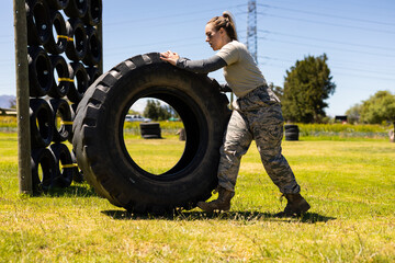 Caucasian female soldier rolling a tire during obstacle course at boot camp