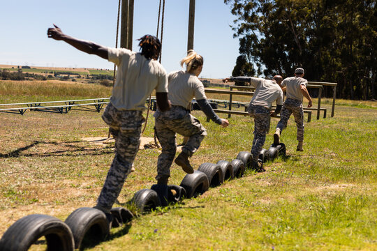 Group of male and female diverse soldiers walking on tires during obstacle course at boot camp