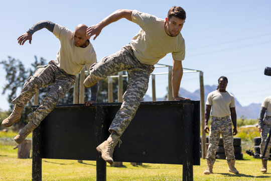 Two diverse male soldiers climbing wooden wall during obstacle course at boot camp