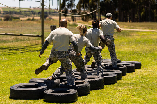 Rear view of group of diverse soldiers walking on tires during obstacle course at boot camp