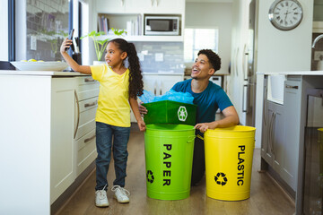 Biracial girl taking selfie with father while recycling waste in kitchen at home