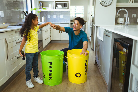 Happy multiracial father and daughter giving fist bump while doing waste management in kitchen