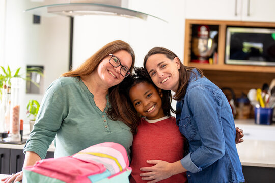 Portrait of smiling mature lesbian couple with happy african american daughter standing at home