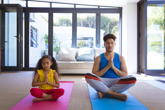 Full length of biracial father and daughter meditating together while practicing yoga at home