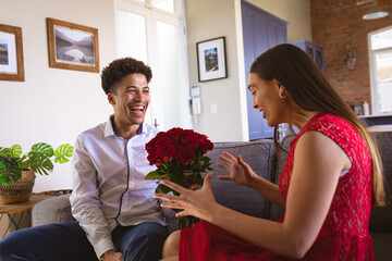 Happy young man giving rose bouquet to surprised girlfriend in living room at home