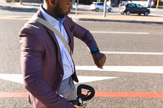 African american businessman with bicycle using smartwatch on the street on the go to office - Powered by Adobe