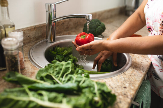 Cropped image of woman washing fresh red bell pepper at sink in kitchen