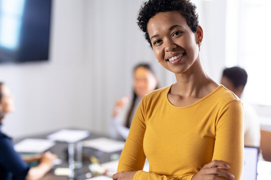 Portrait of confident businesswoman with arms crossed while colleagues discussing in background