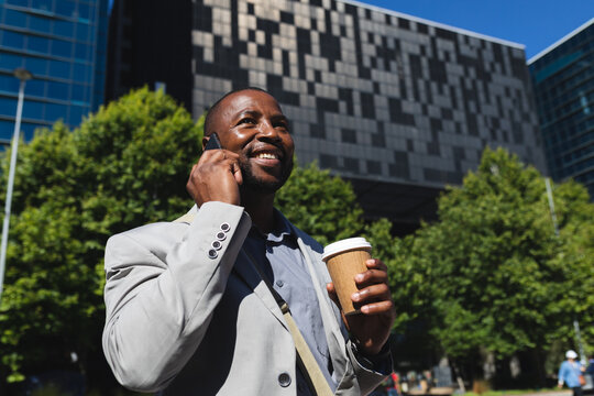 African american businessman with coffee cup talking on smartphone on the street on the go to office
