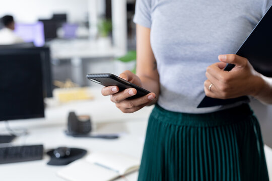 Midsection of businesswoman using smart phone in creative office