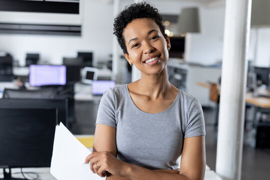 Portrait of smiling biracial businesswoman with documents in creative office