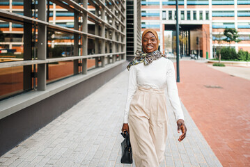 Stylish black Muslim woman with bag observing high buildings