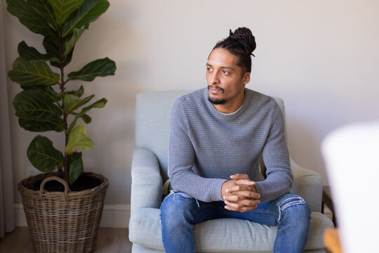 Thoughtful african american young man sitting on a chair at home